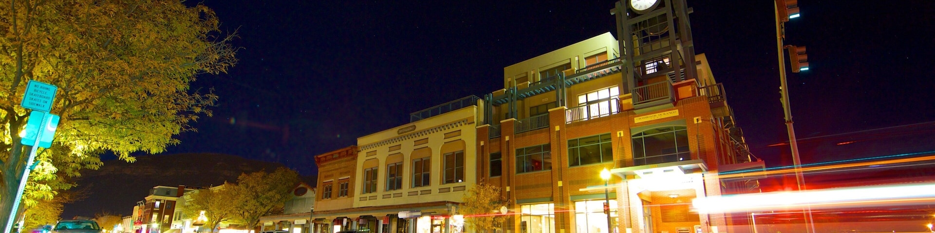 A nighttime street scene with a clock tower, lit-up buildings, and a crosswalk.