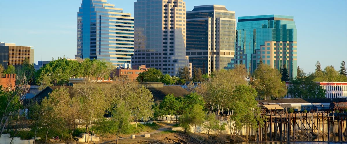 A city skyline with modern buildings and a river in the foreground.