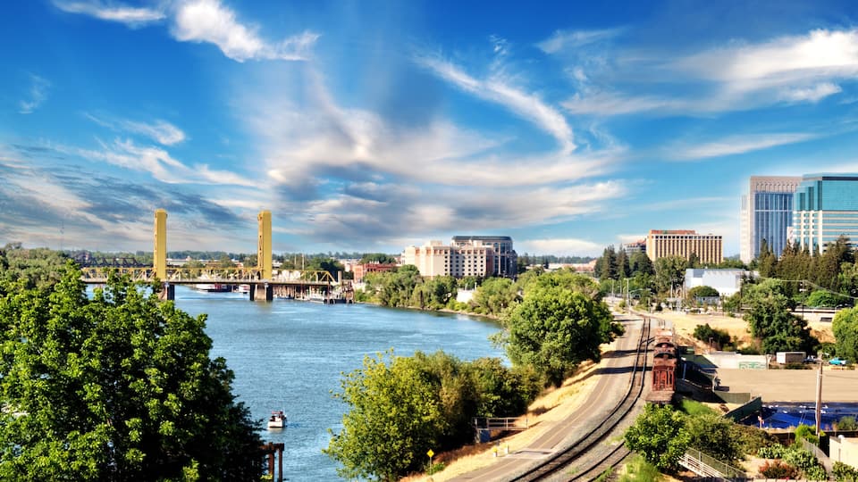 A river with a bridge, a train track, and buildings in the background.
