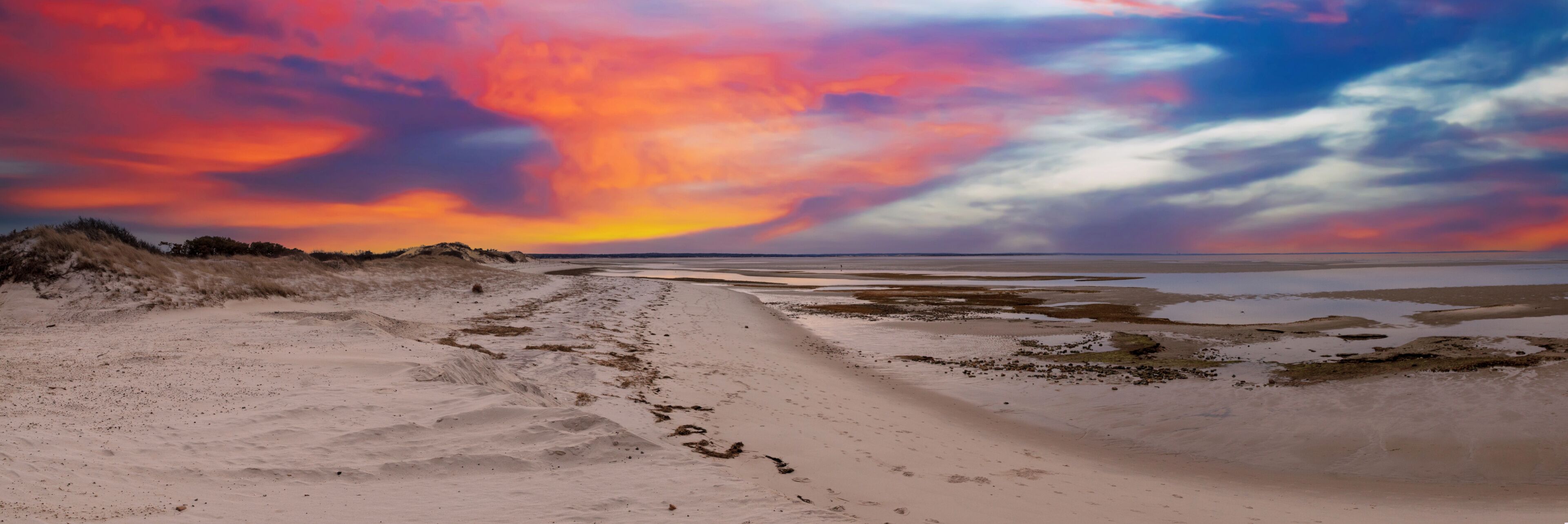 Uma praia com dunas de areia e um céu ao pôr do sol.