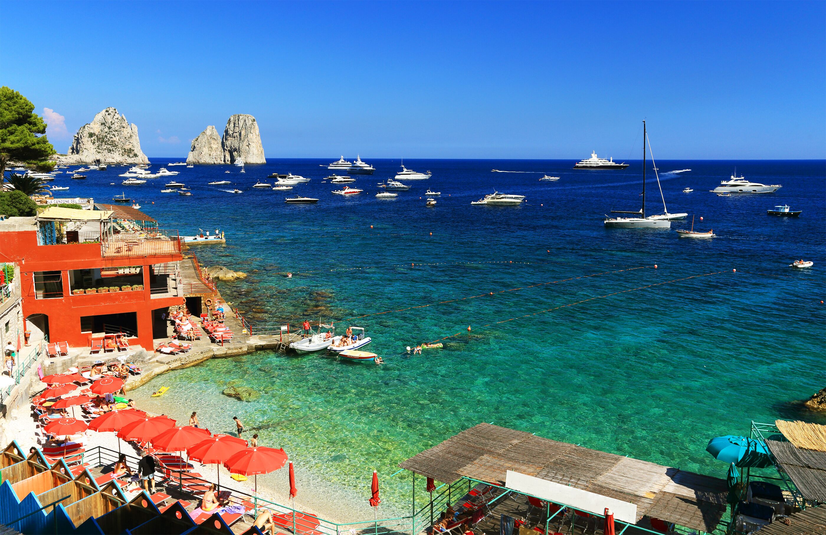 A coastal town with clear turquoise waters, boats, and red umbrellas.