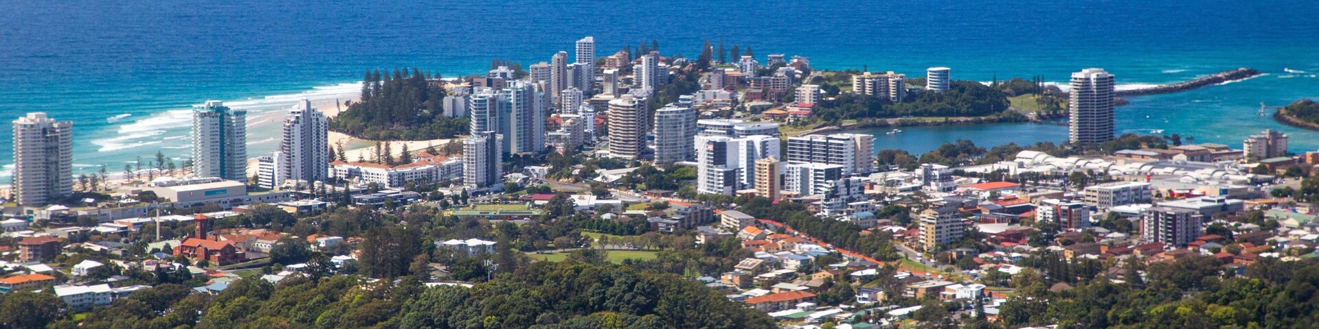 Paisagem costeira com intenso desenvolvimento urbano, uma praia e uma área arborizada.