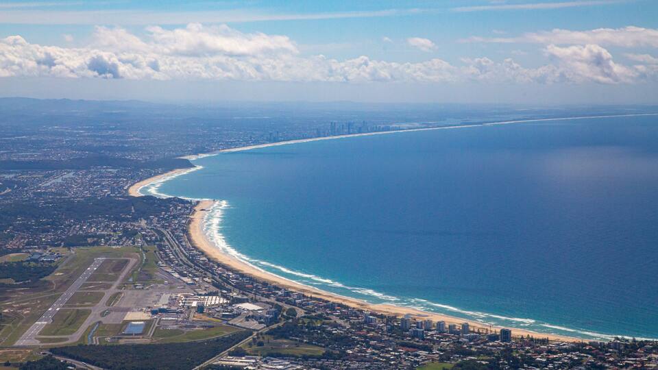 An aerial view of a coastal city with a beach, a dense urban area, and a distant city skyline.