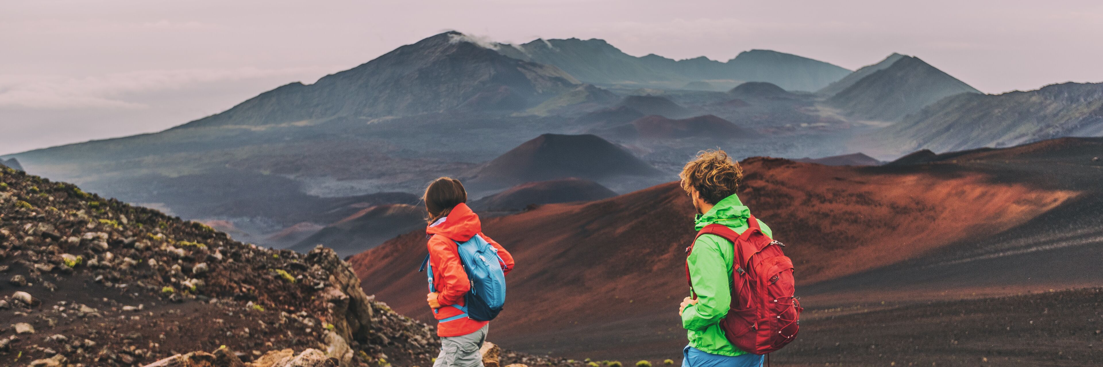 Two hikers on a rocky mountain trail with a view of distant mountains.
