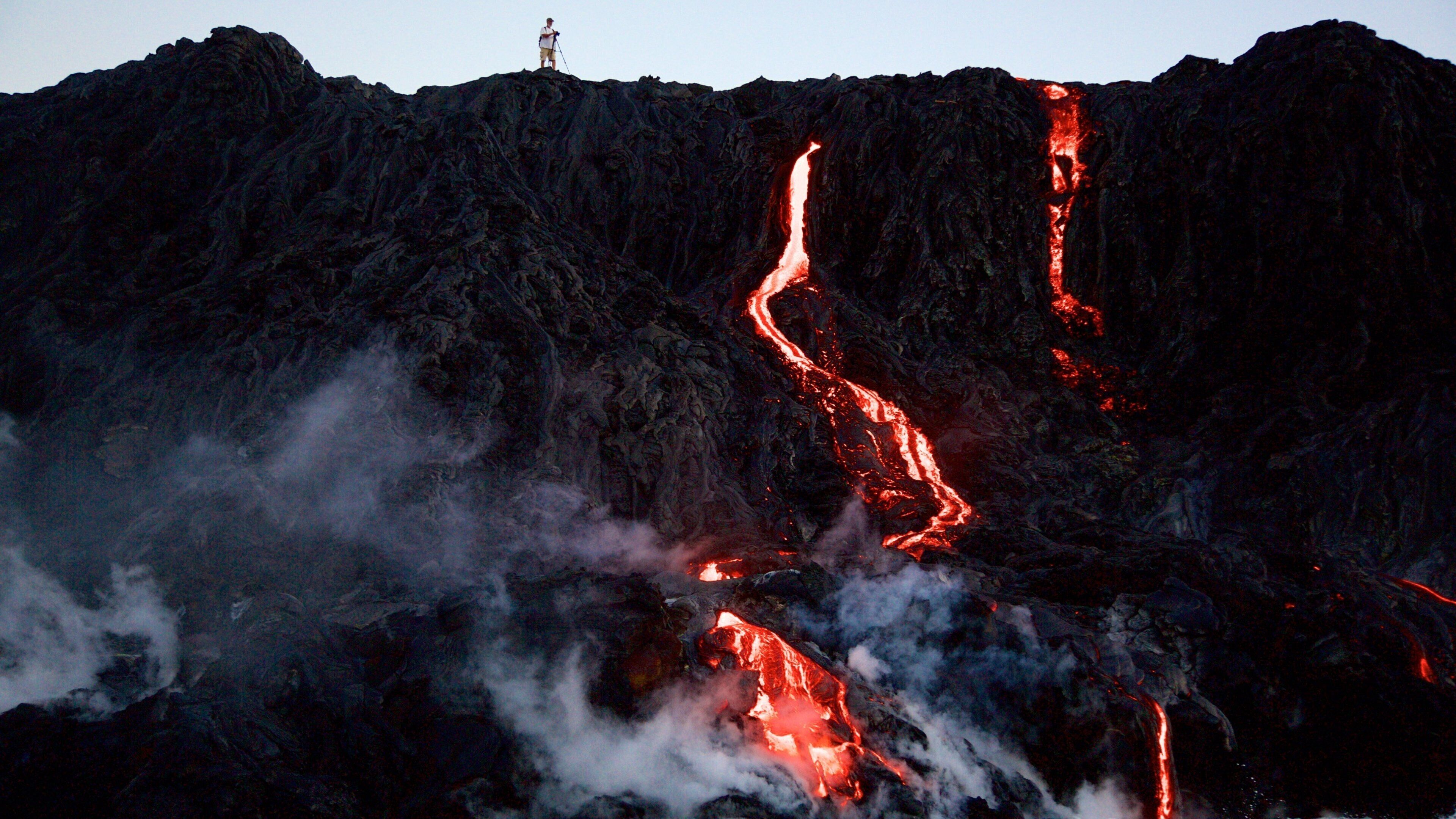 A person standing on a mountain with flowing lava.