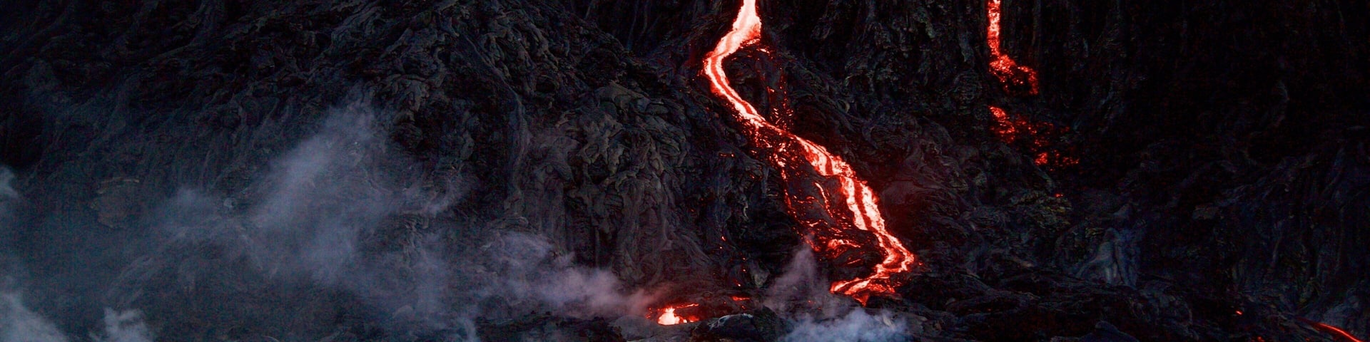A person standing on a mountain with flowing lava.