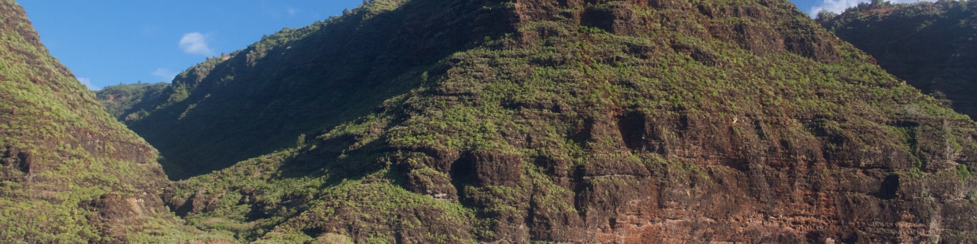 A rugged mountain landscape with lush green vegetation and a clear blue sky.