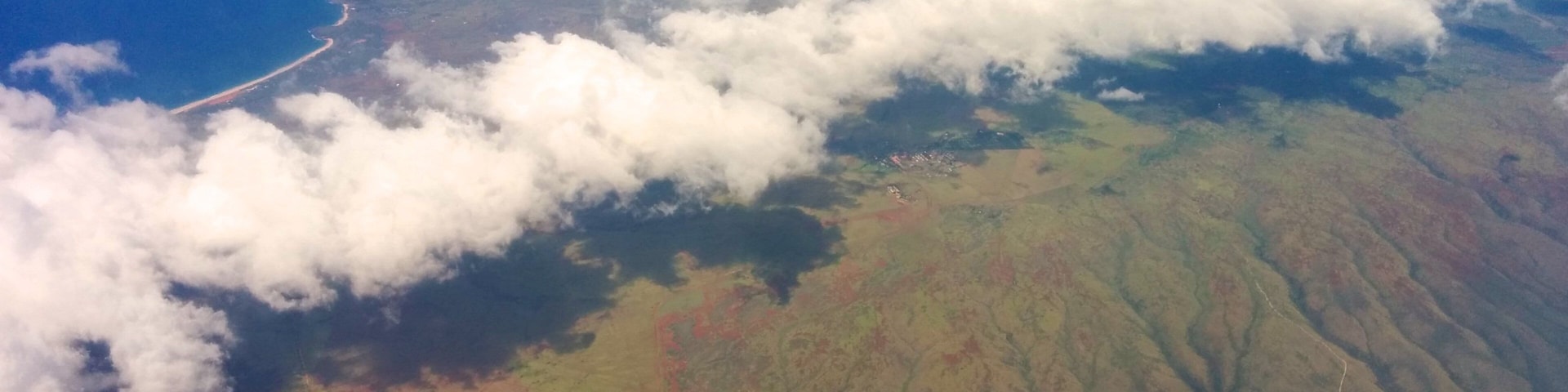 A coastal landscape with a winding road, cloud cover, and a distant shoreline.