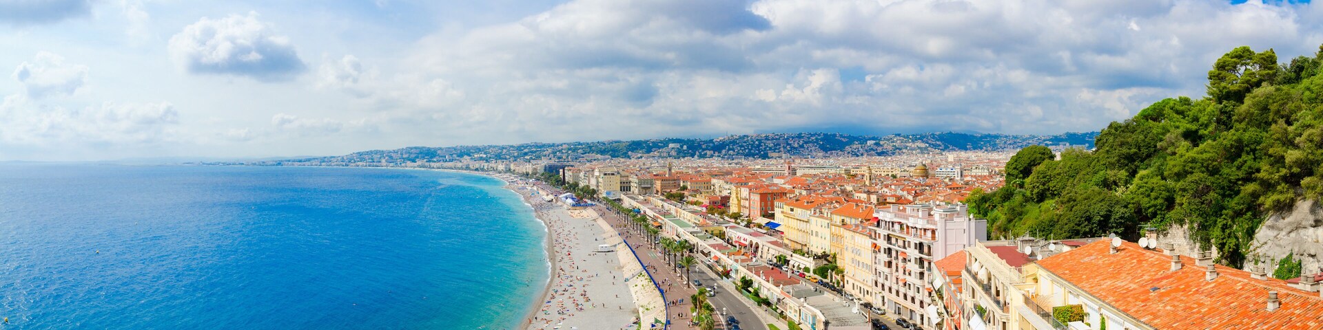 Un paisaje urbano costero con una playa, edificios y una colina con árboles.