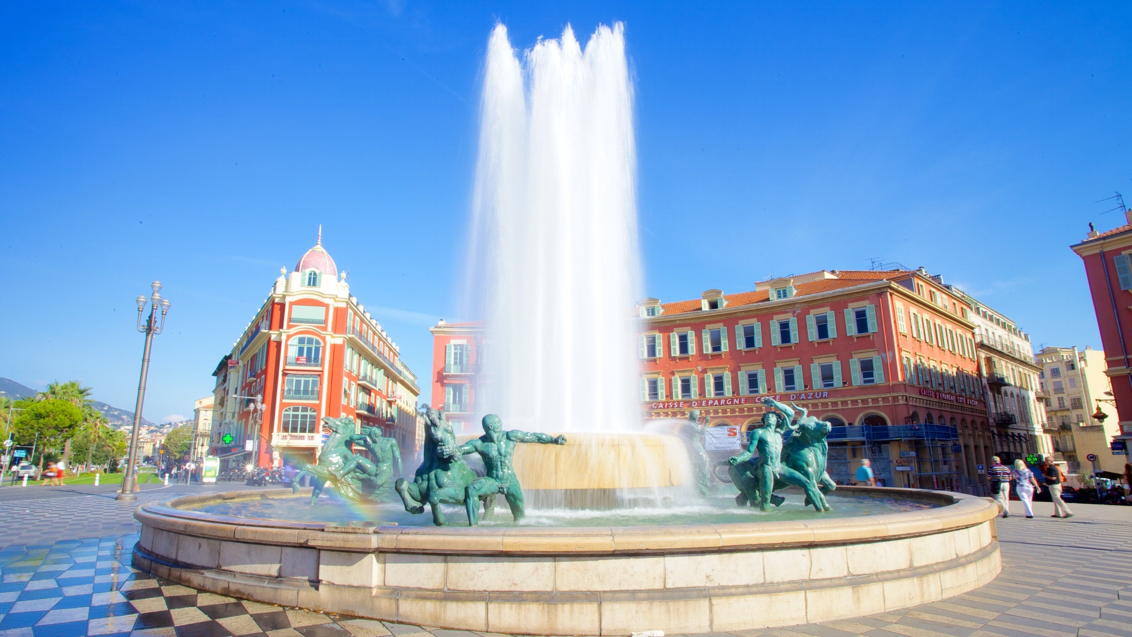 A fountain with statues in a square, surrounded by historic buildings.