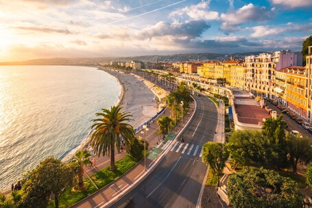Un paysage urbain côtier avec une plage, des palmiers et des bâtiments aux couleurs vives le long du front de mer.