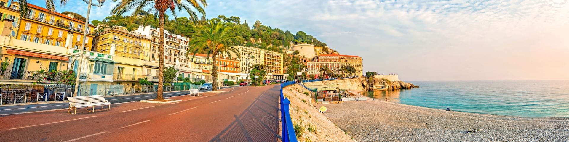 A coastal street with buildings, palm trees, and a beach.
