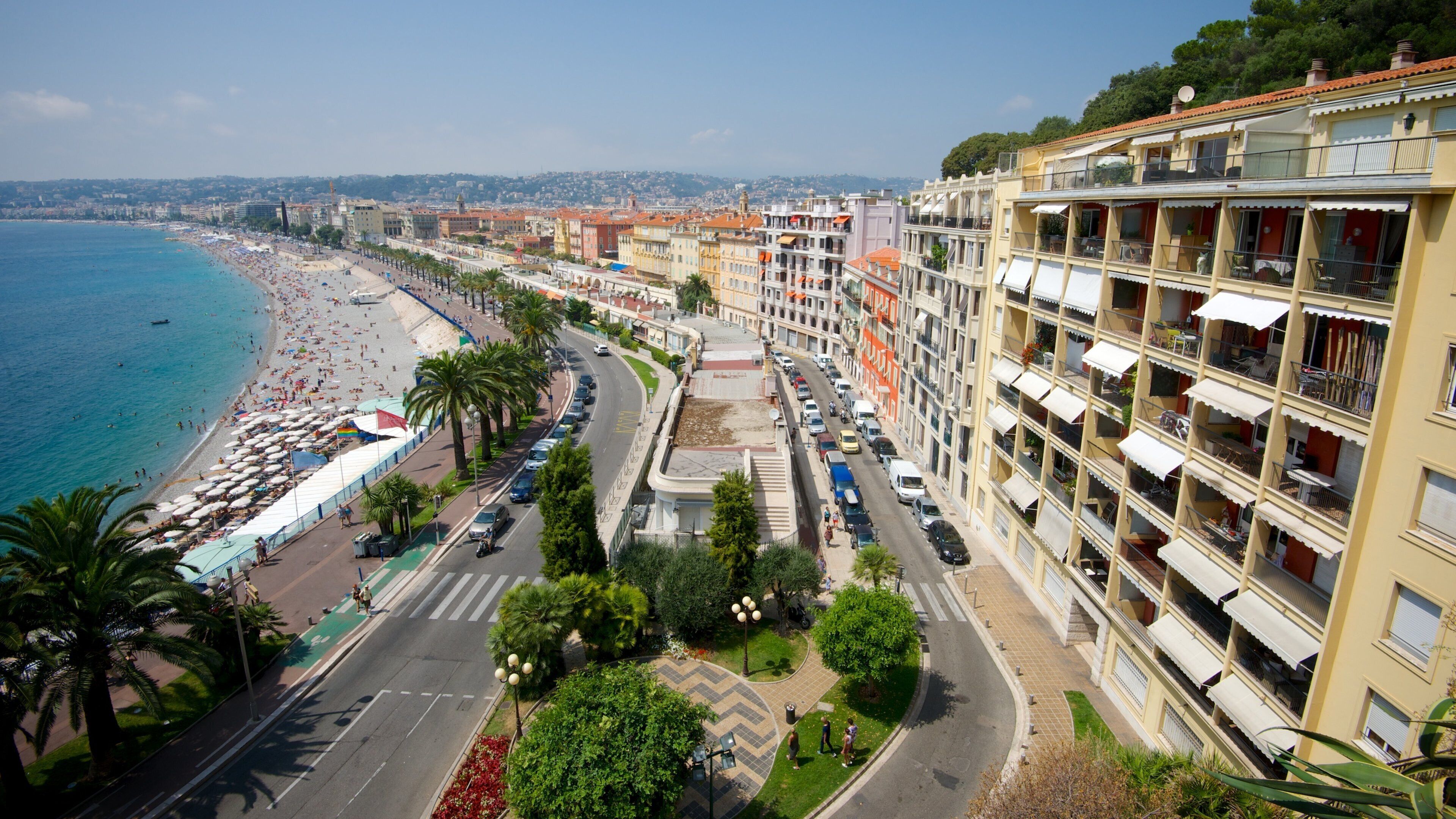 A coastal cityscape with a beach, palm-lined promenade, and colorful buildings.