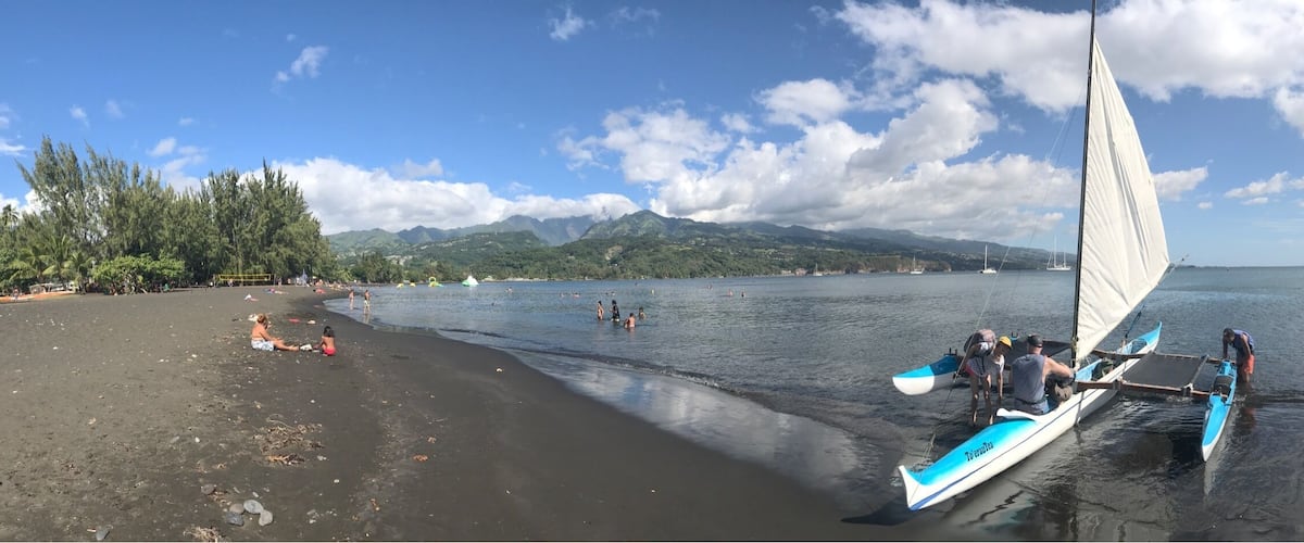 A beach with people swimming and a sailboat near the shore.