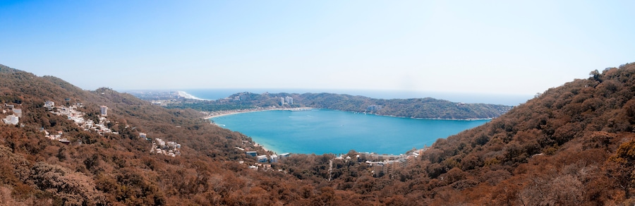 Un paisaje costero con una bahía rodeada de colinas, edificios y densos bosques.