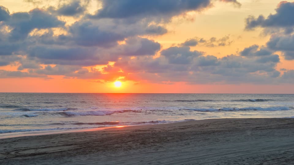 A sunset over the ocean with waves on the shore.