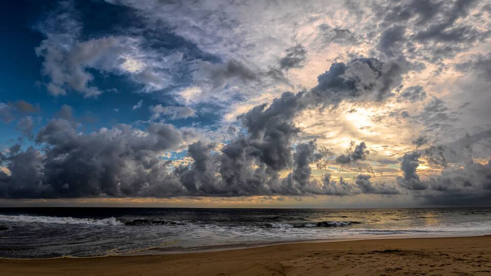 A beach with waves and a cloudy sky.