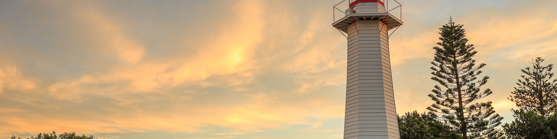 Un faro con una parte superior roja, rodeado de árboles y un área verde.