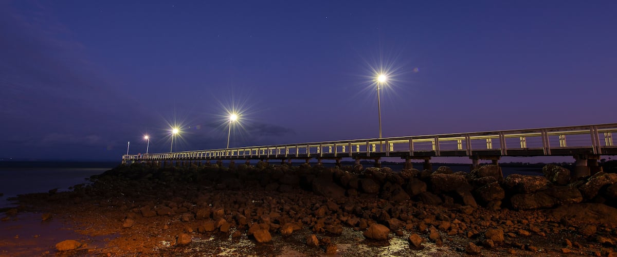 A bridge over a rocky shoreline at night with streetlights.