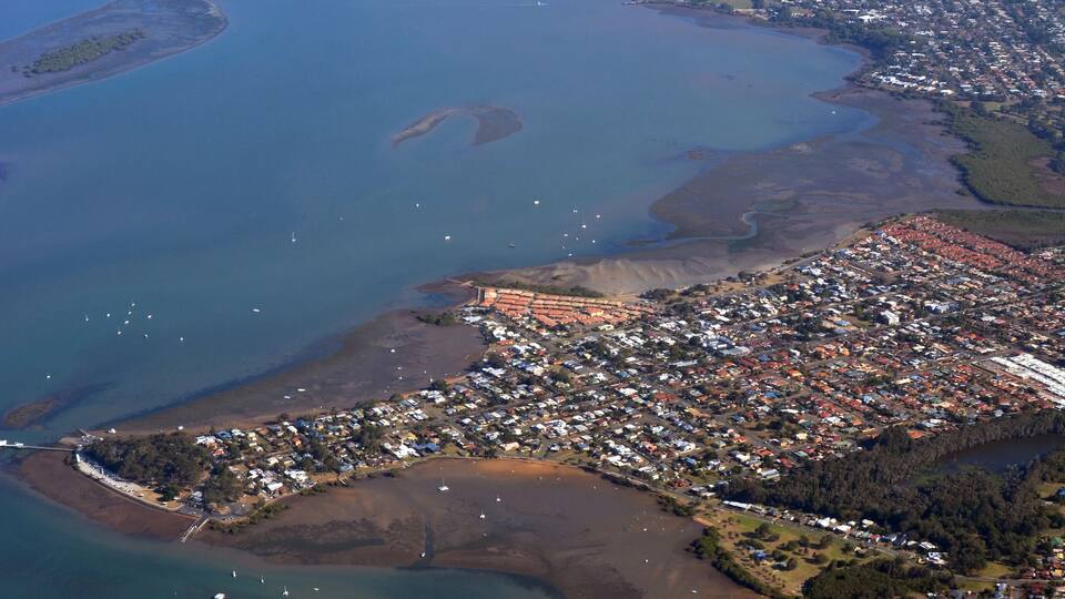 An aerial view of a coastal town with a marina, residential areas, and surrounding water bodies.
