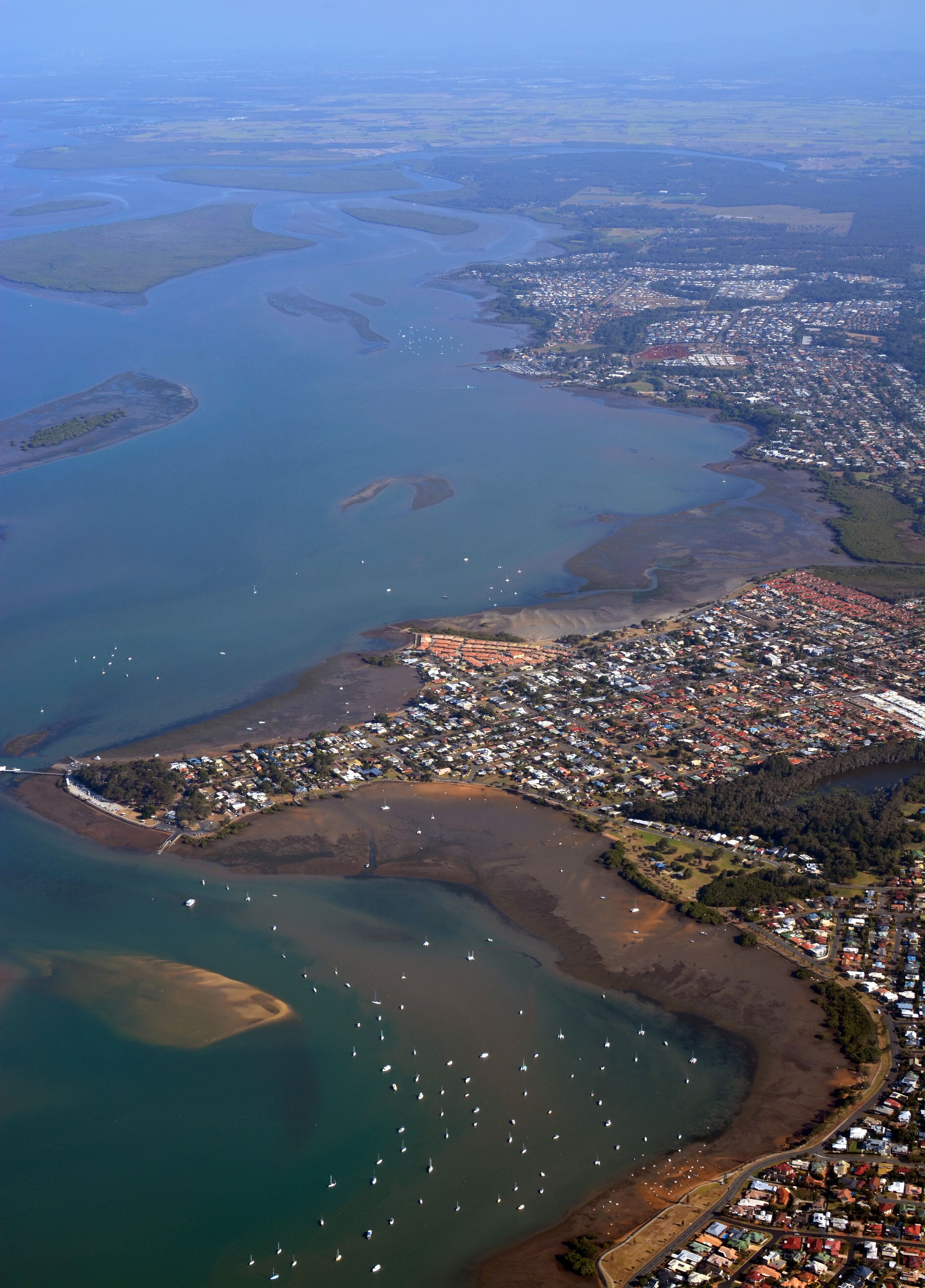 An aerial view of a coastal town with a marina, residential areas, and surrounding water bodies.