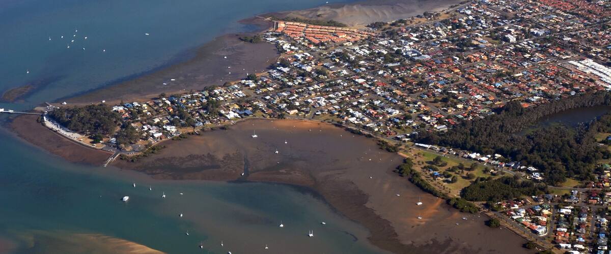 An aerial view of a coastal town with a marina, residential areas, and surrounding water bodies.