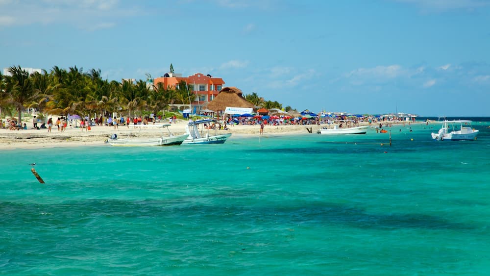 A beach with turquoise waters, boats, and a crowd of people.