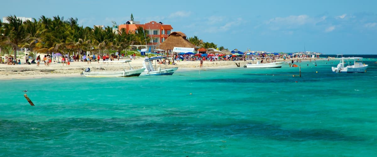 A beach with turquoise waters, boats, and a crowd of people.