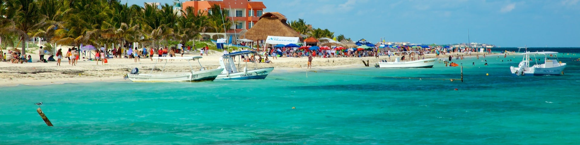 A beach with turquoise waters, boats, and a crowd of people.