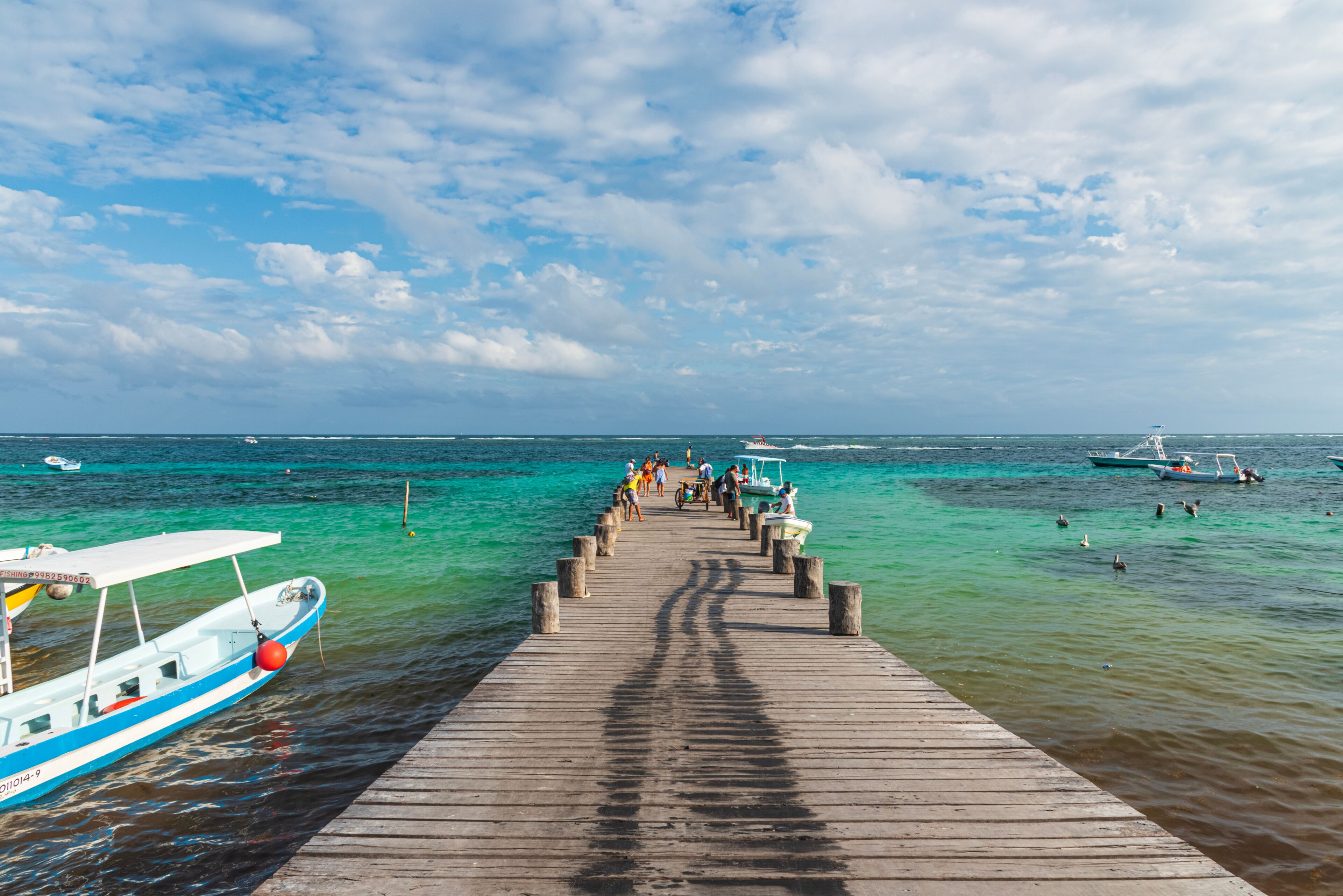 A wooden pier extending into turquoise waters with boats docked on either side.