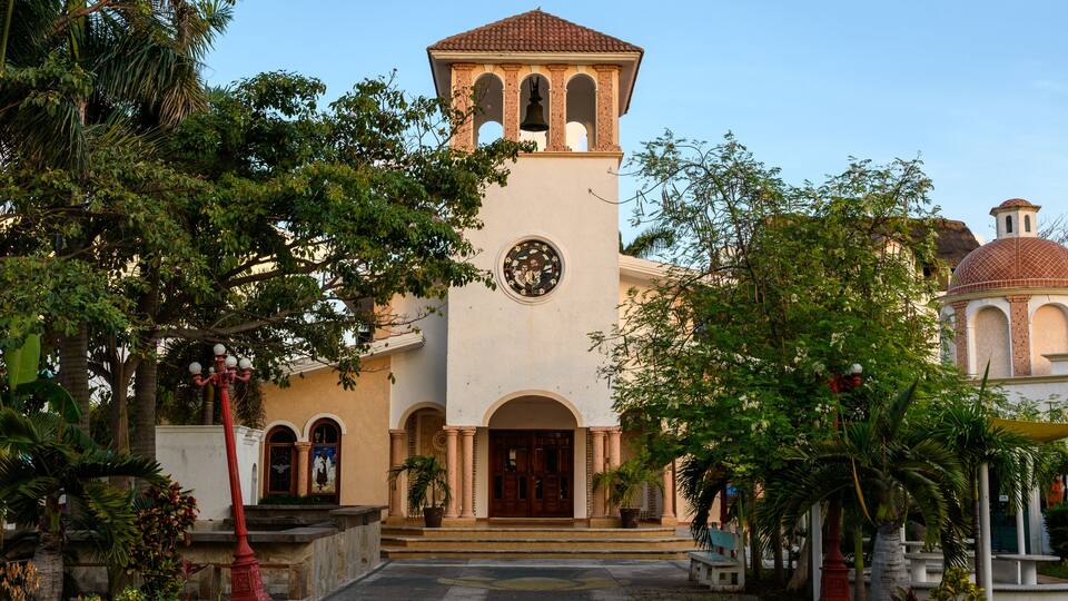 A historic building with a clock tower, arched doorways, and a garden with palm trees.