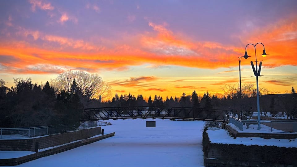 A snow-covered bridge at sunset with a colorful sky.
