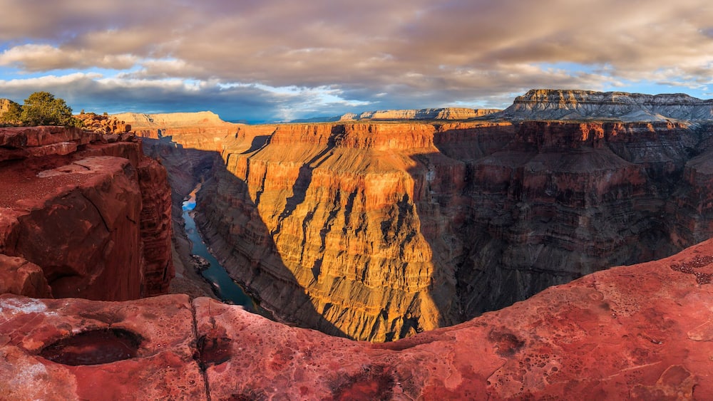 A deep canyon with red rock formations and a river running through it.