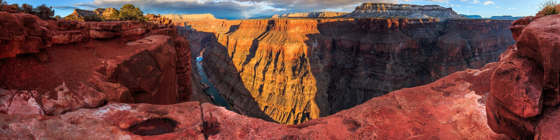 A deep canyon with red rock formations and a river running through it.