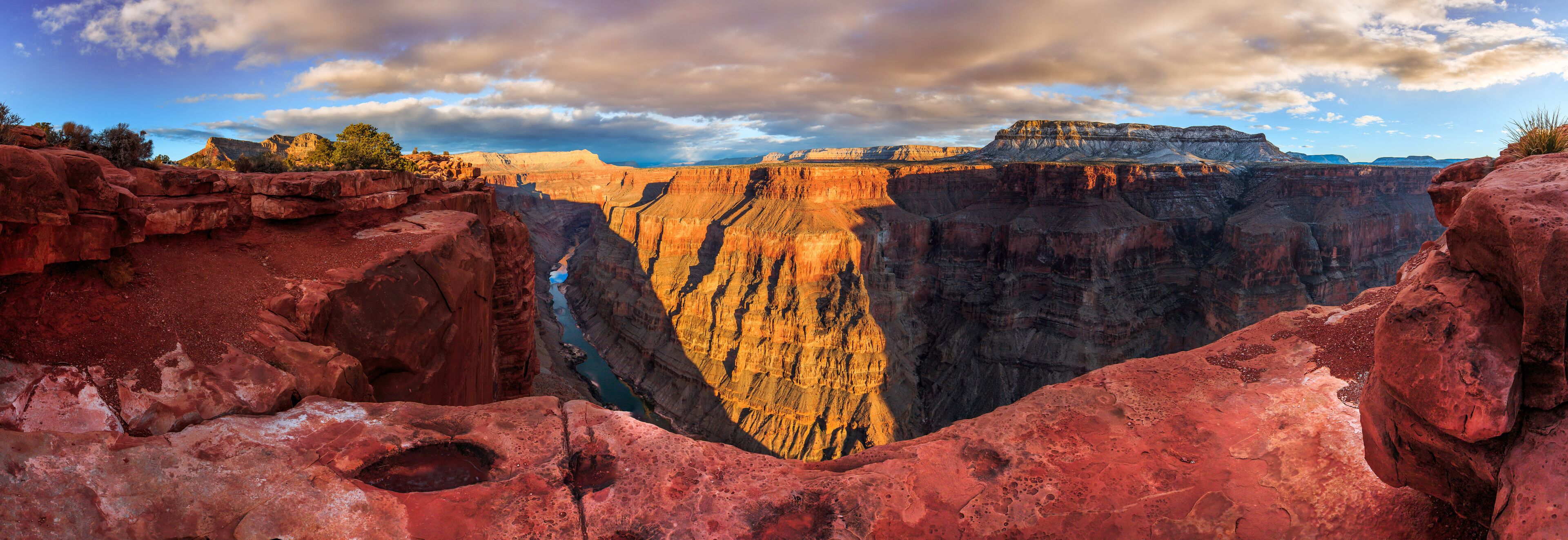 A deep canyon with red rock formations and a river running through it.