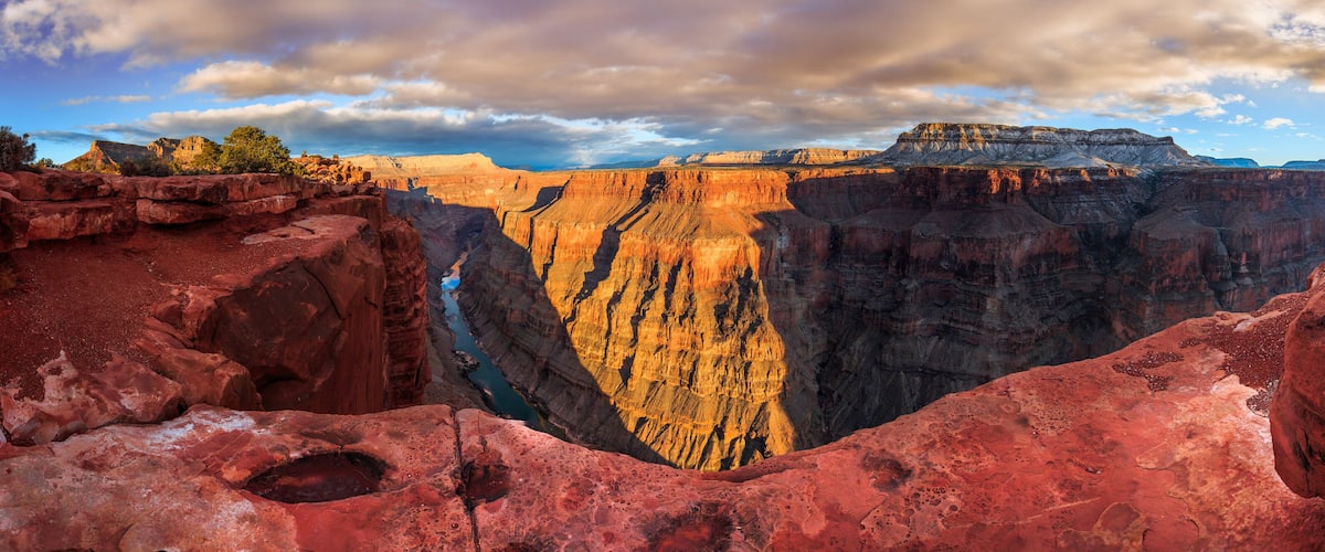 A deep canyon with red rock formations and a river running through it.