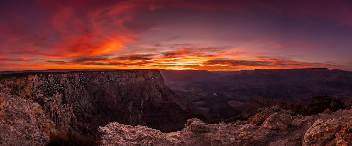 A canyon with layered rock formations and a sunset sky.