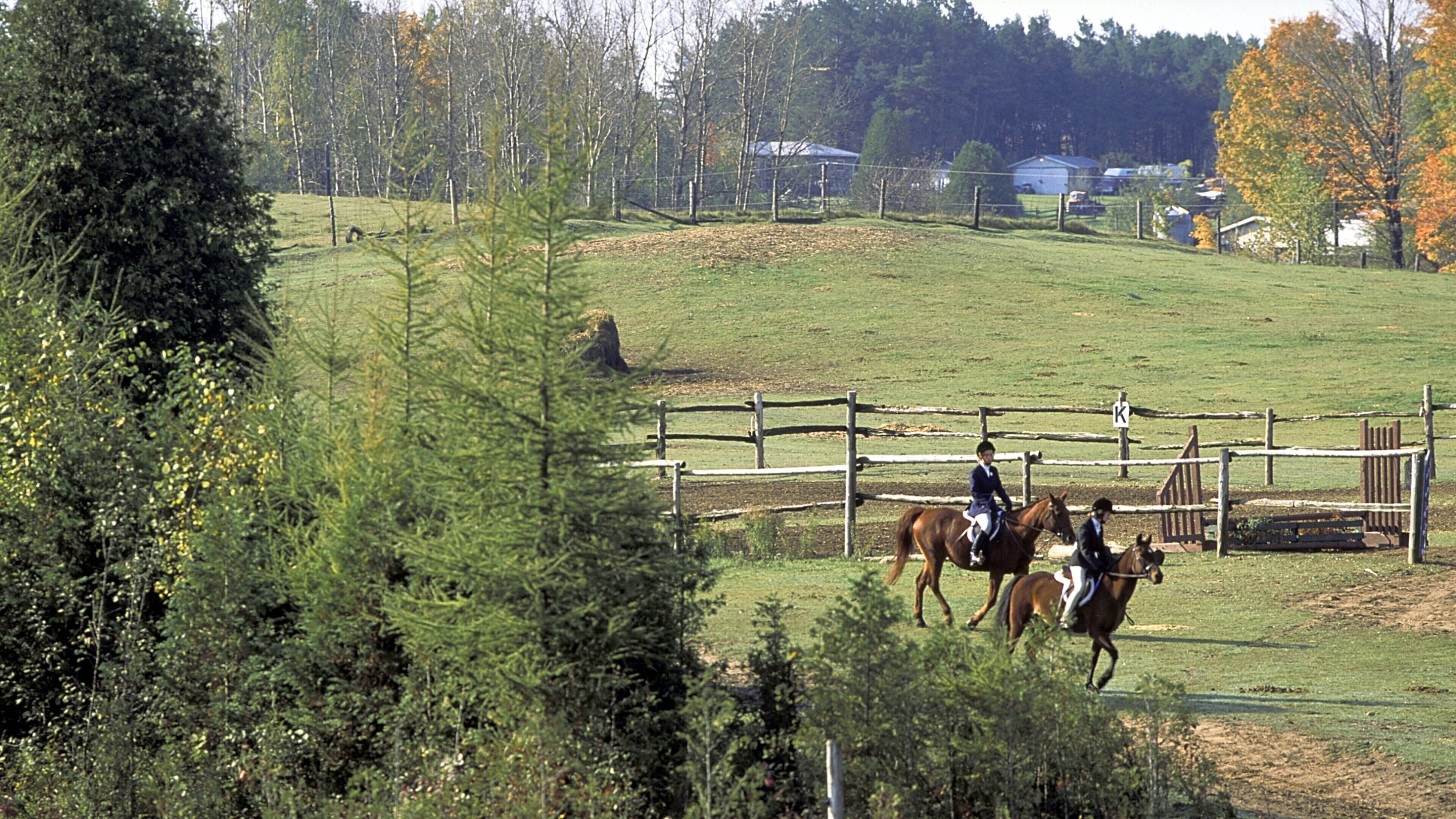 A fenced equestrian area with riders on horses.