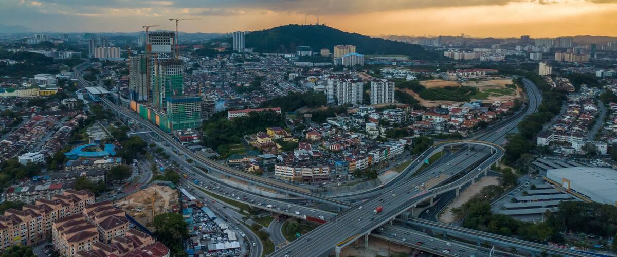 A cityscape with a prominent skyscraper under construction, a dense residential area, and a complex highway interchange.