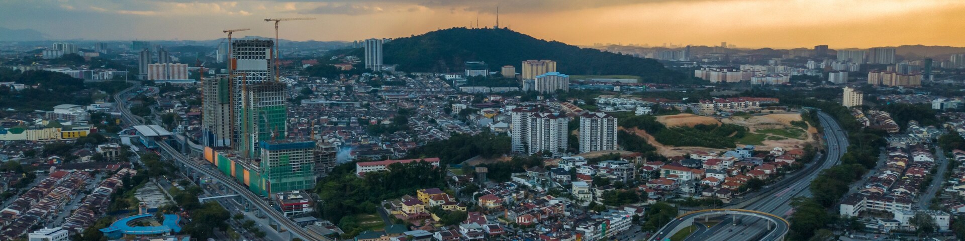 A cityscape with a prominent skyscraper under construction, a dense residential area, and a complex highway interchange.