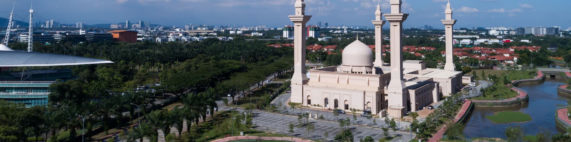 A mosque with three minarets, surrounded by a water feature and palm trees.