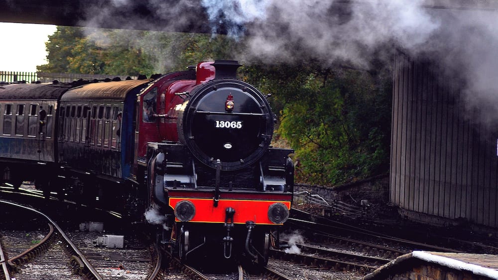 A steam locomotive numbered 13065 on tracks with a bridge overhead.