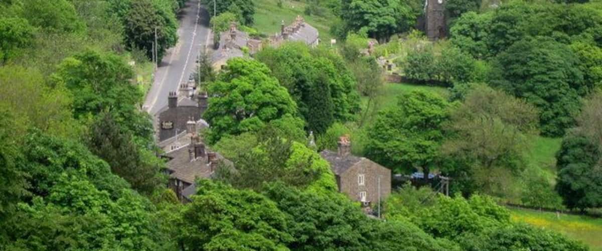 Holcombe Village. The village of Holcombe is in the middle of all the trees with 330268 on the right. The village occupies a picturesque position on the slopes of Holcombe Hill. The buildings in the area are predominantly made up of stone cottages a public house, a restaurant, church and primary school. At one time the village also boasted a shop, post office, and a regular bus service linking it to Holcombe Brook, a neighbouring village in the valley bottom one mile to the south. The main road to the left is Helmshore Road with the sign on wall of 444148 in the foreground.