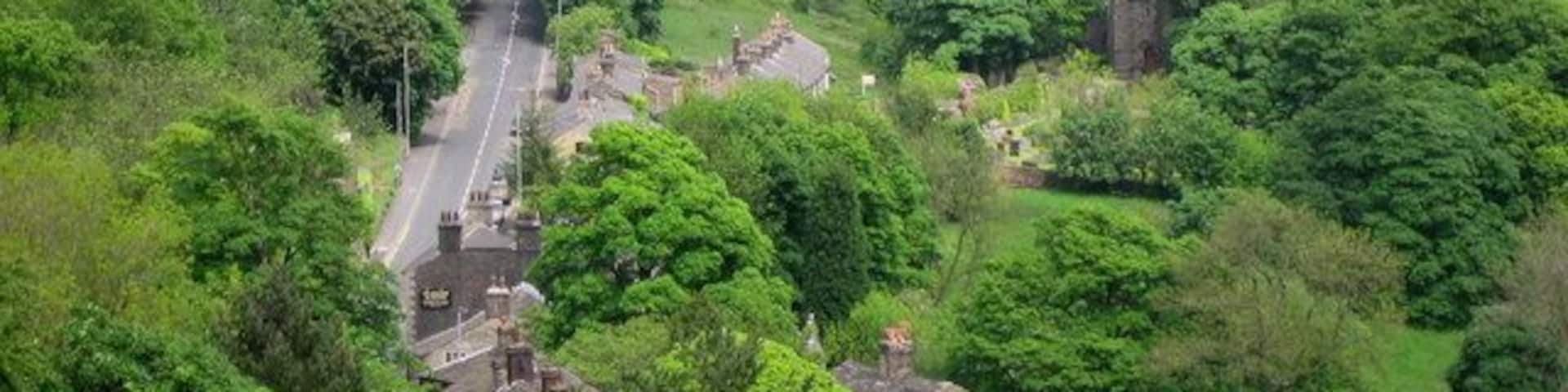 Holcombe Village. The village of Holcombe is in the middle of all the trees with 330268 on the right. The village occupies a picturesque position on the slopes of Holcombe Hill. The buildings in the area are predominantly made up of stone cottages a public house, a restaurant, church and primary school. At one time the village also boasted a shop, post office, and a regular bus service linking it to Holcombe Brook, a neighbouring village in the valley bottom one mile to the south. The main road to the left is Helmshore Road with the sign on wall of 444148 in the foreground.