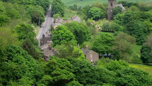 Holcombe Village. The village of Holcombe is in the middle of all the trees with 330268 on the right. The village occupies a picturesque position on the slopes of Holcombe Hill. The buildings in the area are predominantly made up of stone cottages a public house, a restaurant, church and primary school. At one time the village also boasted a shop, post office, and a regular bus service linking it to Holcombe Brook, a neighbouring village in the valley bottom one mile to the south. The main road to the left is Helmshore Road with the sign on wall of 444148 in the foreground.