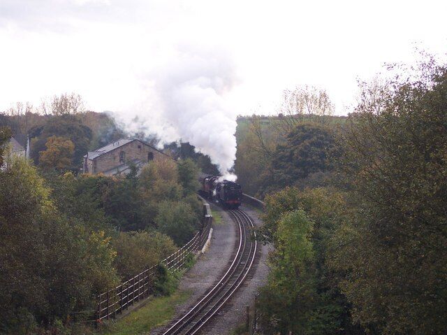 A steam train on tracks surrounded by trees and a building.