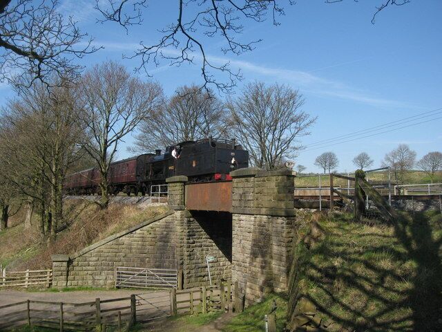 Un tren cruzando un puente de piedra sobre un río, rodeado de árboles y un cielo despejado.