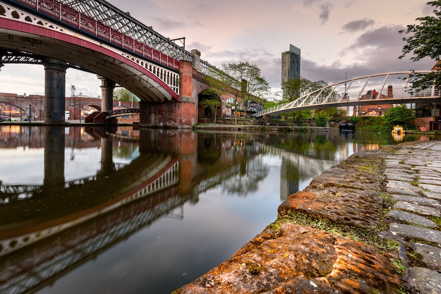 Un río con un puente, un muro de piedra y un edificio moderno al fondo.