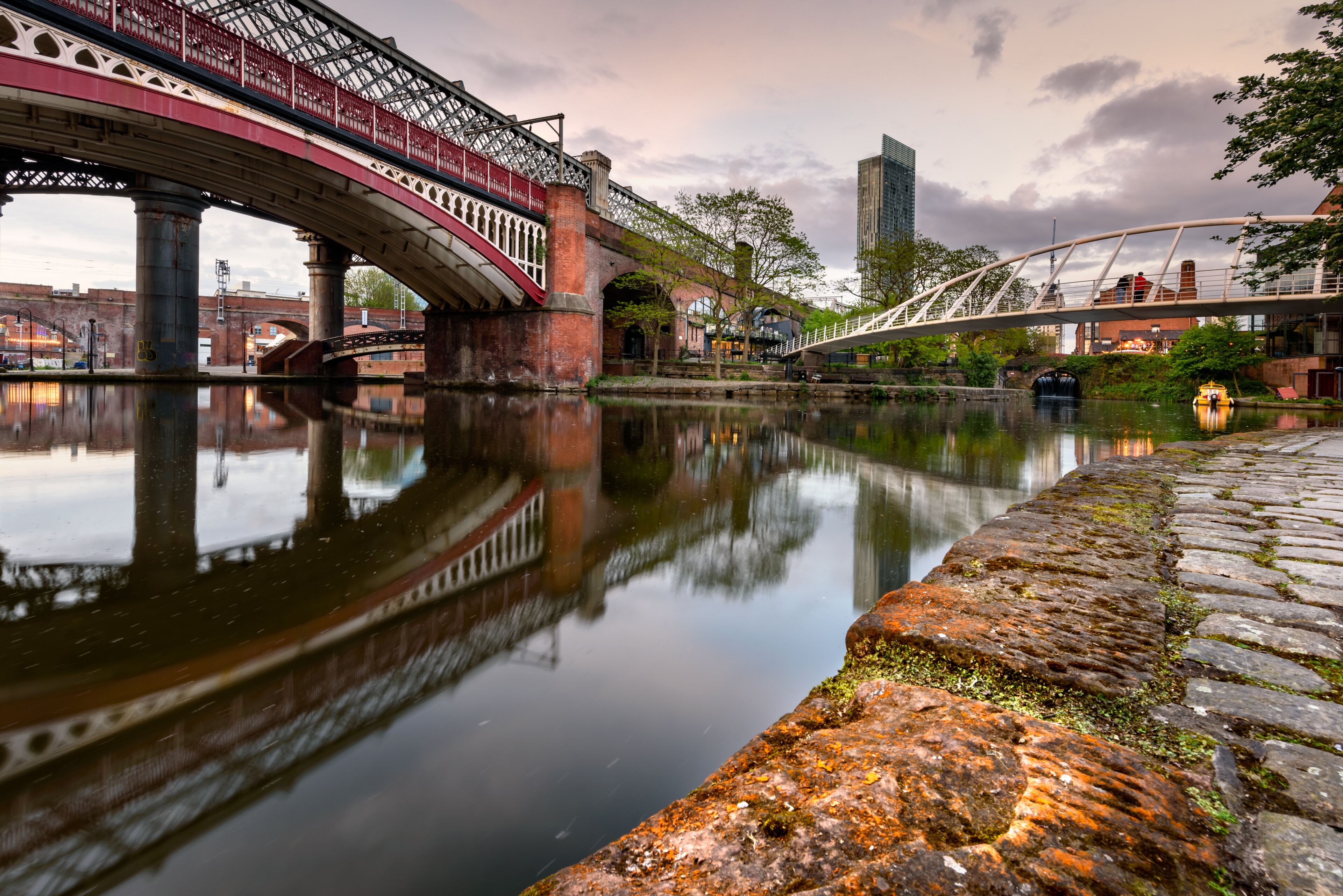 A river with a bridge, stone wall, and a modern building in the background.