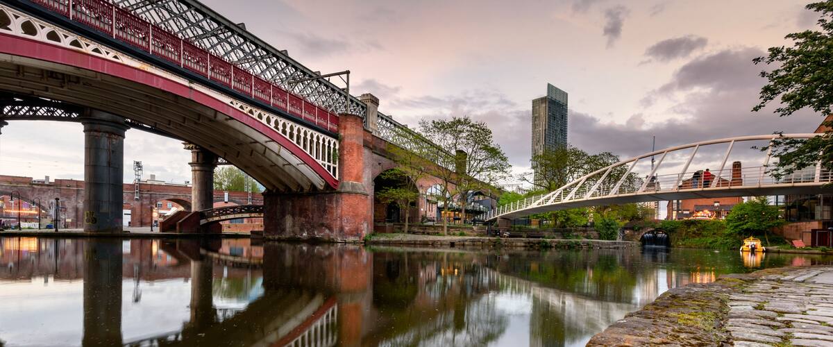 A river with a bridge, stone wall, and a modern building in the background.